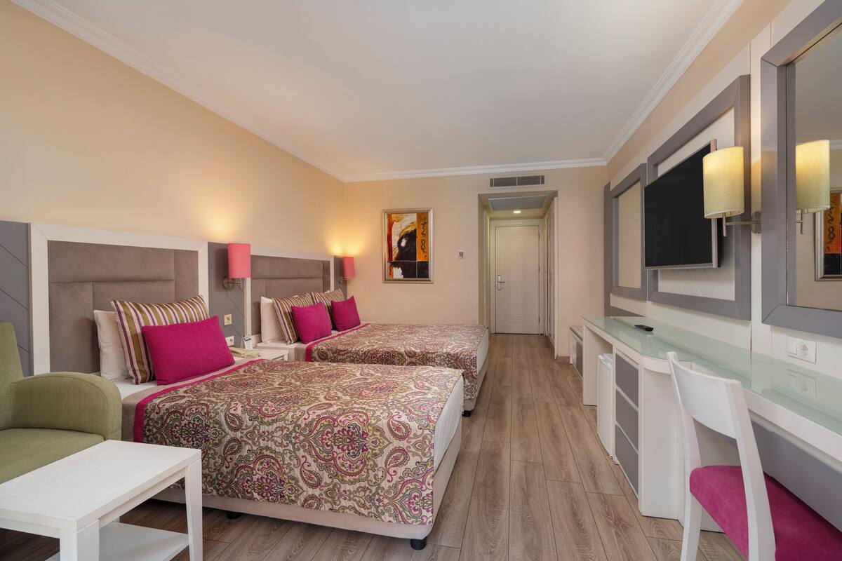A hotel room with two beds, a desk, a chair, and a TV.