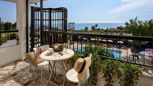 A balcony with a table and chairs, a view of the sea, and a pool area. - Titan Club Hotel Ultra All Inclusive (Alanya)