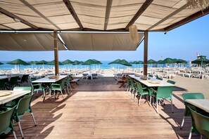 A beachside restaurant with outdoor seating, tables, and umbrellas, overlooking the sea. - Titan Club Hotel Ultra All Inclusive (Alanya)