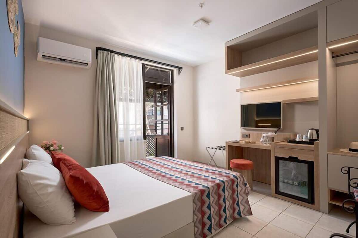 A hotel room with a bed, a desk, a chair, an air conditioning unit, and a television.