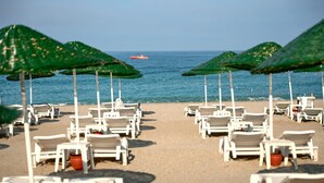 A beach with rows of white lounge chairs and green umbrellas, a boat in the distance, and a clear view of the sea. - Titan Club Hotel Ultra All Inclusive (Alanya)
