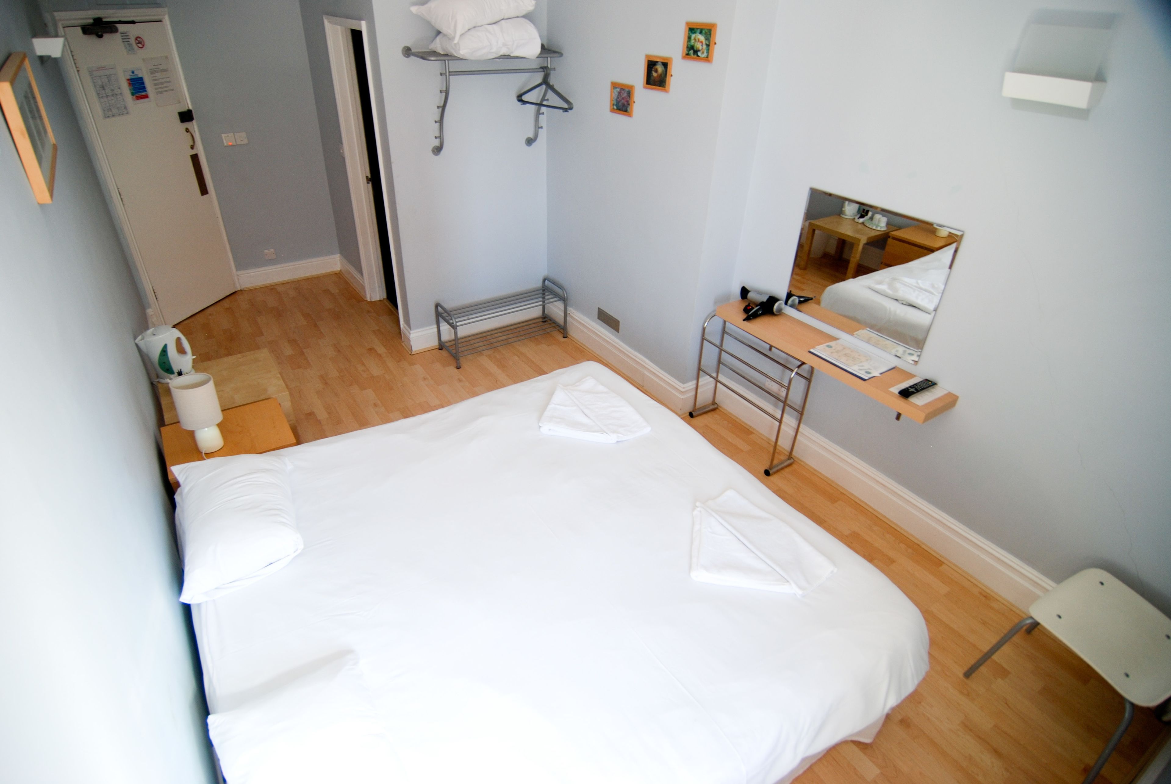 A hotel room with a large bed, a desk with a chair, a mirror, and a wardrobe.