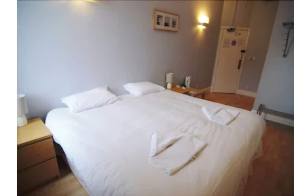 Cama bem arrumada com lençóis brancos e toalhas dobradas no pé.
