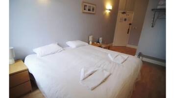 Een opgemaakt bed met witte lakens en handdoeken gevouwen aan het voeteneinde.