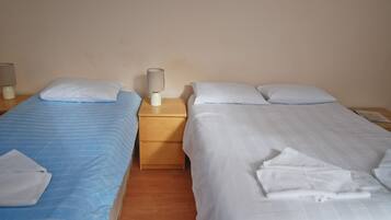 A hotel room with two beds, each with a pillow and a folded towel. There is a nightstand with a lamp between the beds.