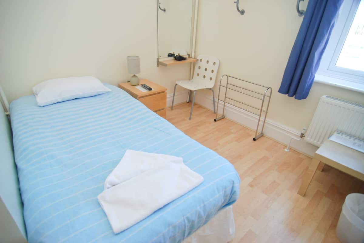 Quarto com cama, poltrona, mesa de cabeceira, espelho e janela com cortinas.