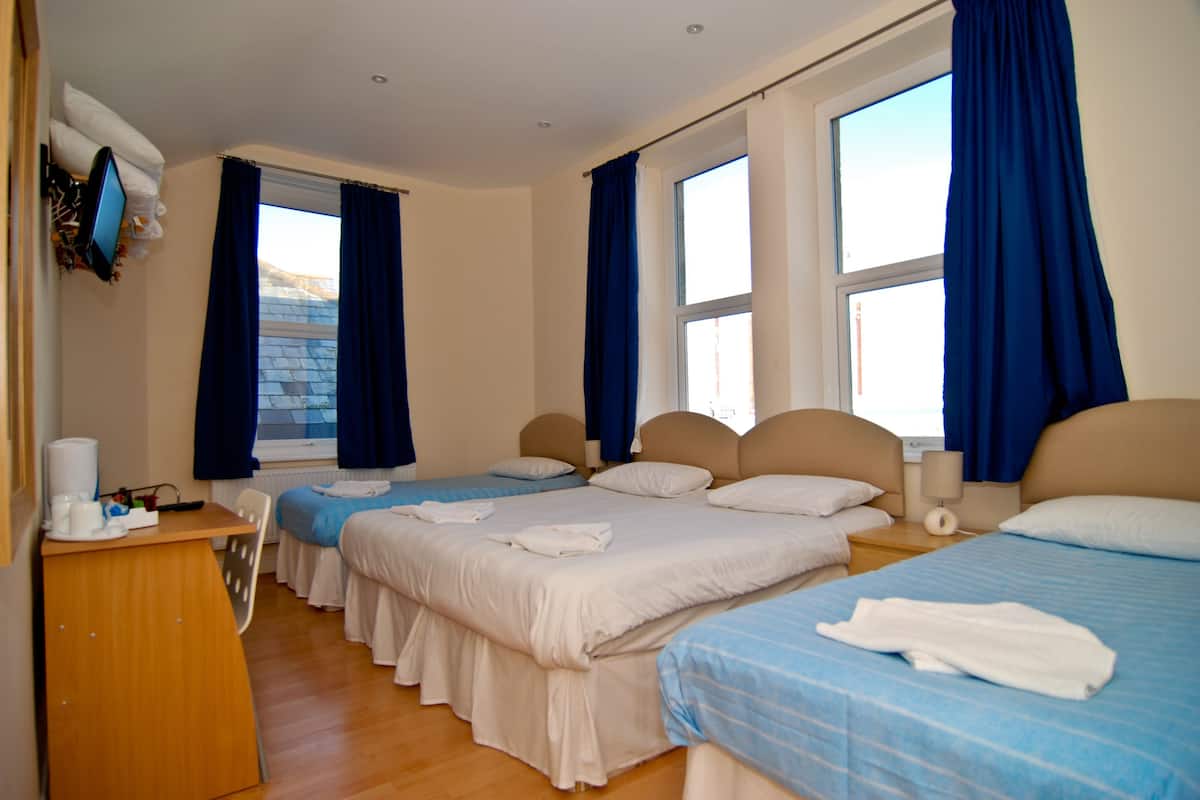 Quarto de hotel com três camas, uma escrivaninha e uma televisão.