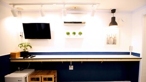 Une cuisine compacte dotée d’un réfrigérateur encastré, d’une table en bois, d’un banc, d’un téléviseur fixé au mur et d’une petite étagère où sont disposés des objets décoratifs.