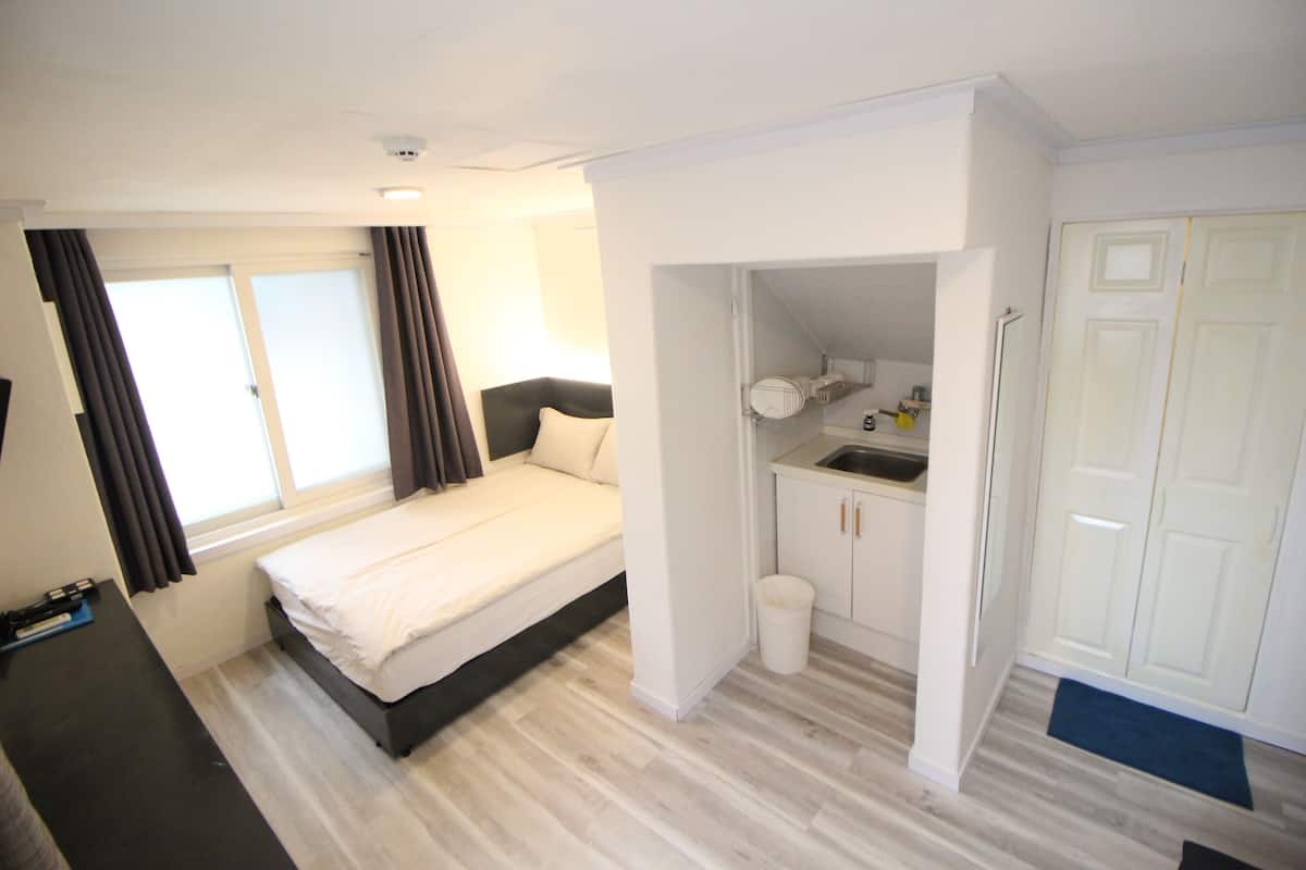 Une chambre d’hôtel de taille réduite comprenant un lit, une petite kitchenette, une salle de bain et un placard.
