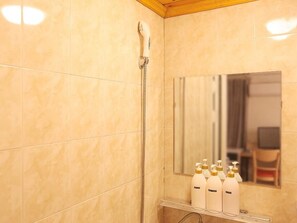 A bathroom with a shower, a mirror, and a shelf with toiletries.