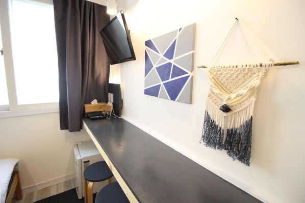Een kamer met een lange donkerhouten tafel, twee kleine ronde krukjes, een flatscreen-tv aan de muur en een wanddecoratie van macramé.