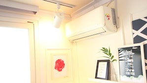 Une pièce avec une porte blanche, un appareil de climatisation, un tableau représentant une rose rouge, une citation encadrée et une plante en pot posée sur une étagère.