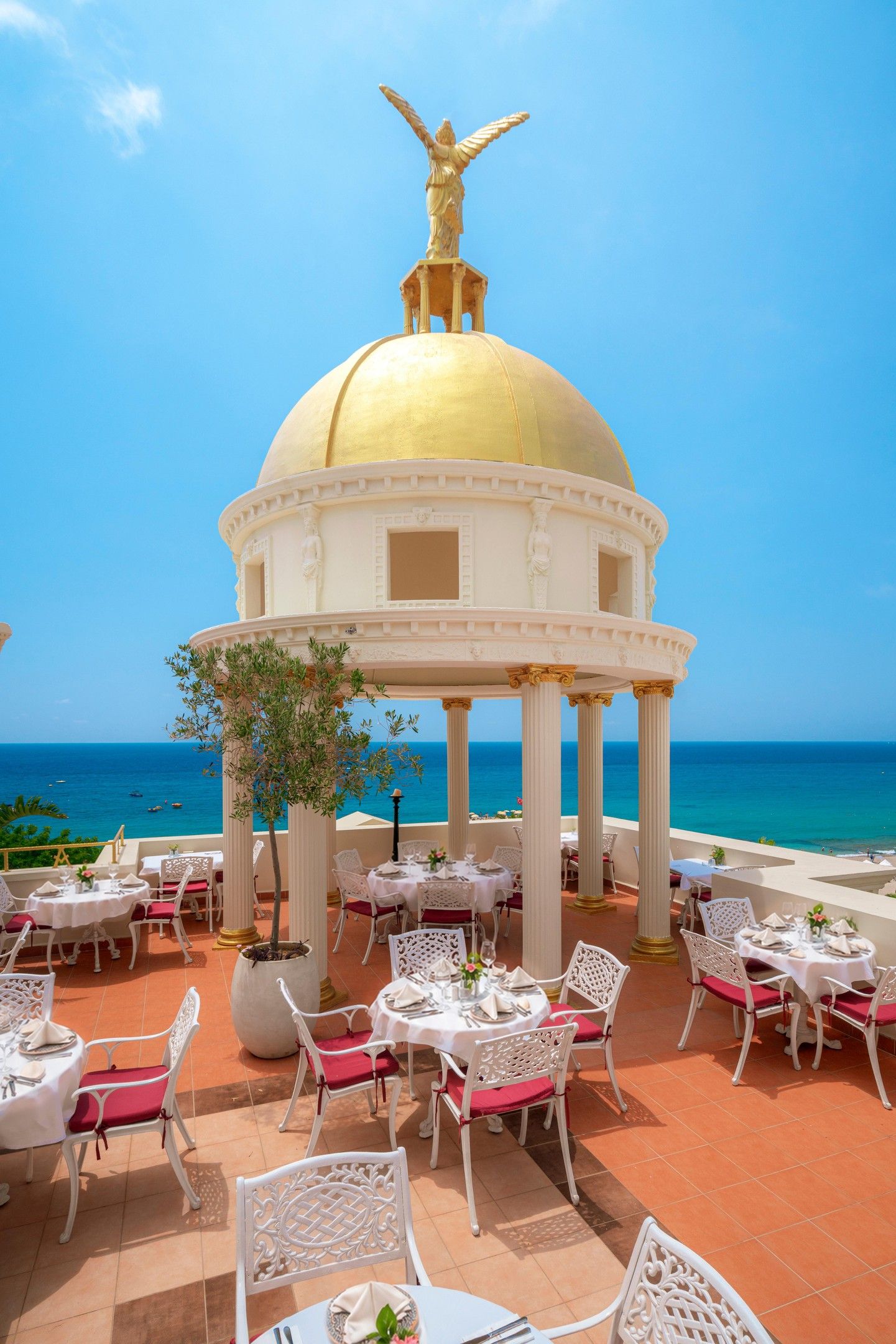 A restaurant with outdoor seating overlooking the sea, featuring a golden dome structure and white columns.