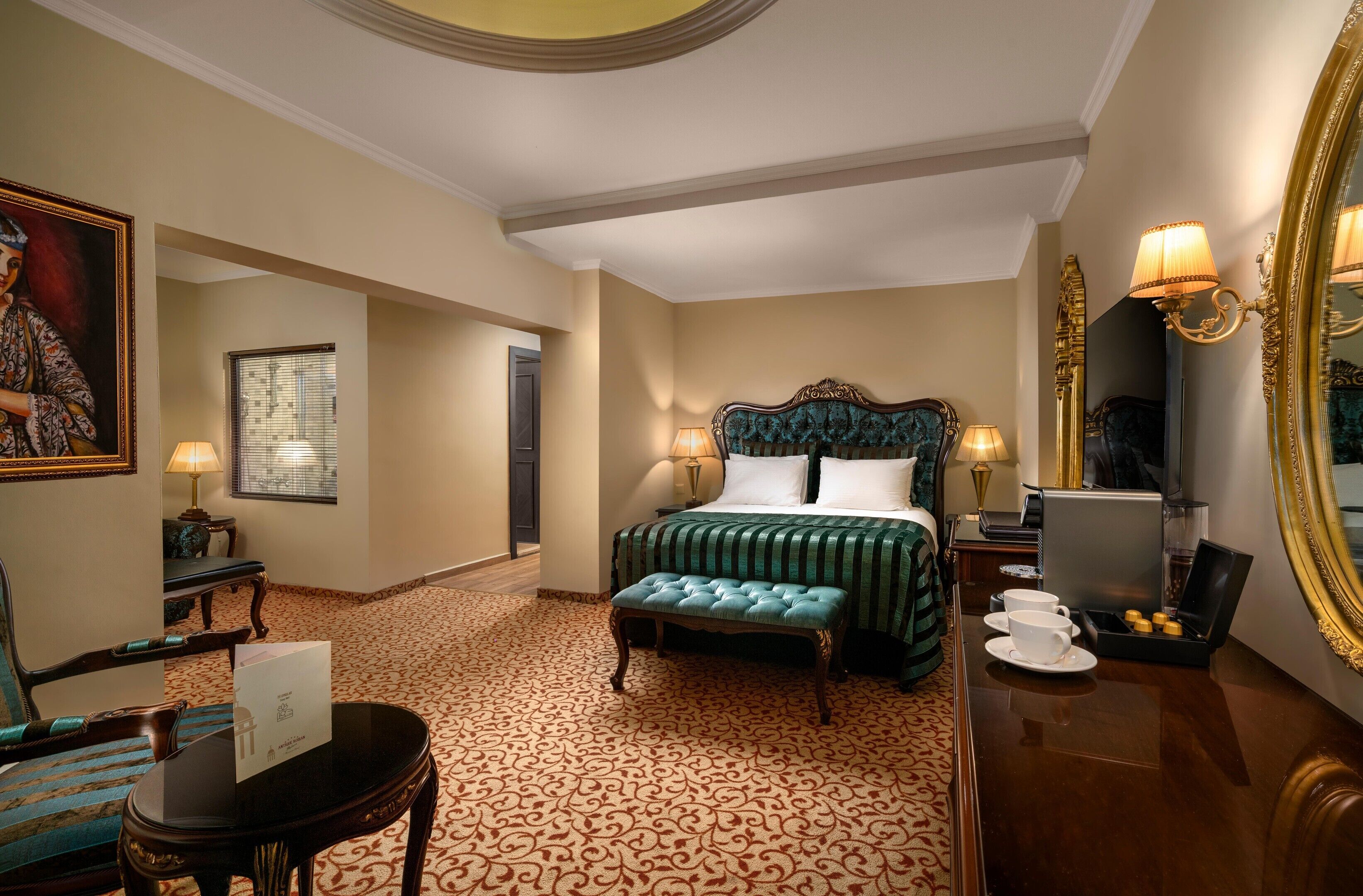 A hotel room with a large bed, a sitting area with a chair and table, a mirror, and a coffee machine.
