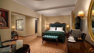 A hotel room with a large bed, a sitting area with a chair and table, a mirror, and a coffee machine.