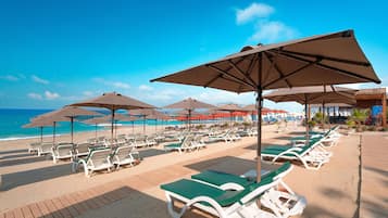 Un complexe hôtelier situé en bord de mer, avec des rangées de chaises longues et de parasols, une terrasse en bois et une vue sur l’océan.