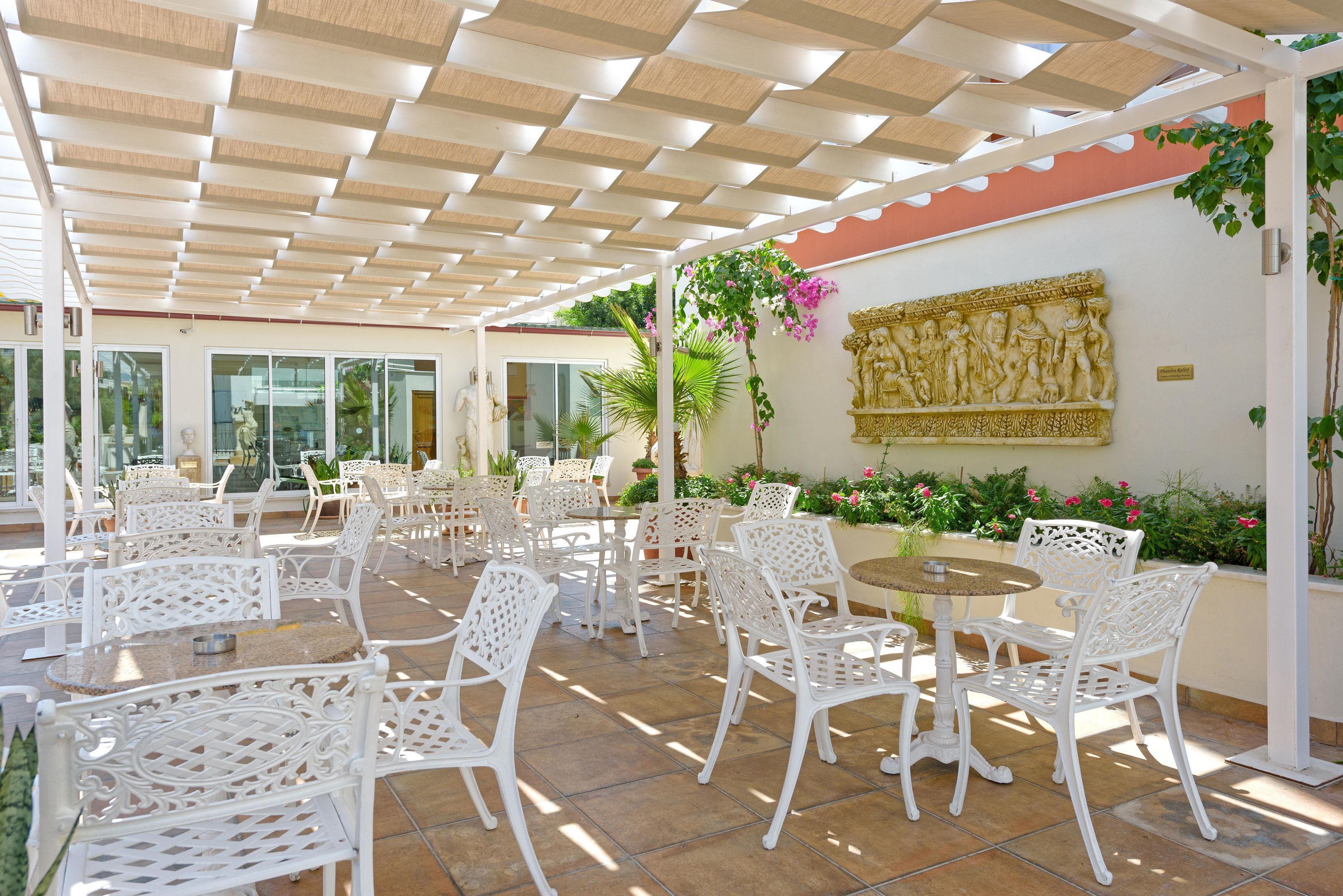 Un patio al aire libre con mobiliario de mimbre blanco, suelo de piedra y una pared decorativa con un relieve.