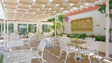 Un patio al aire libre con mobiliario de mimbre blanco, suelo de piedra y una pared decorativa con un relieve.