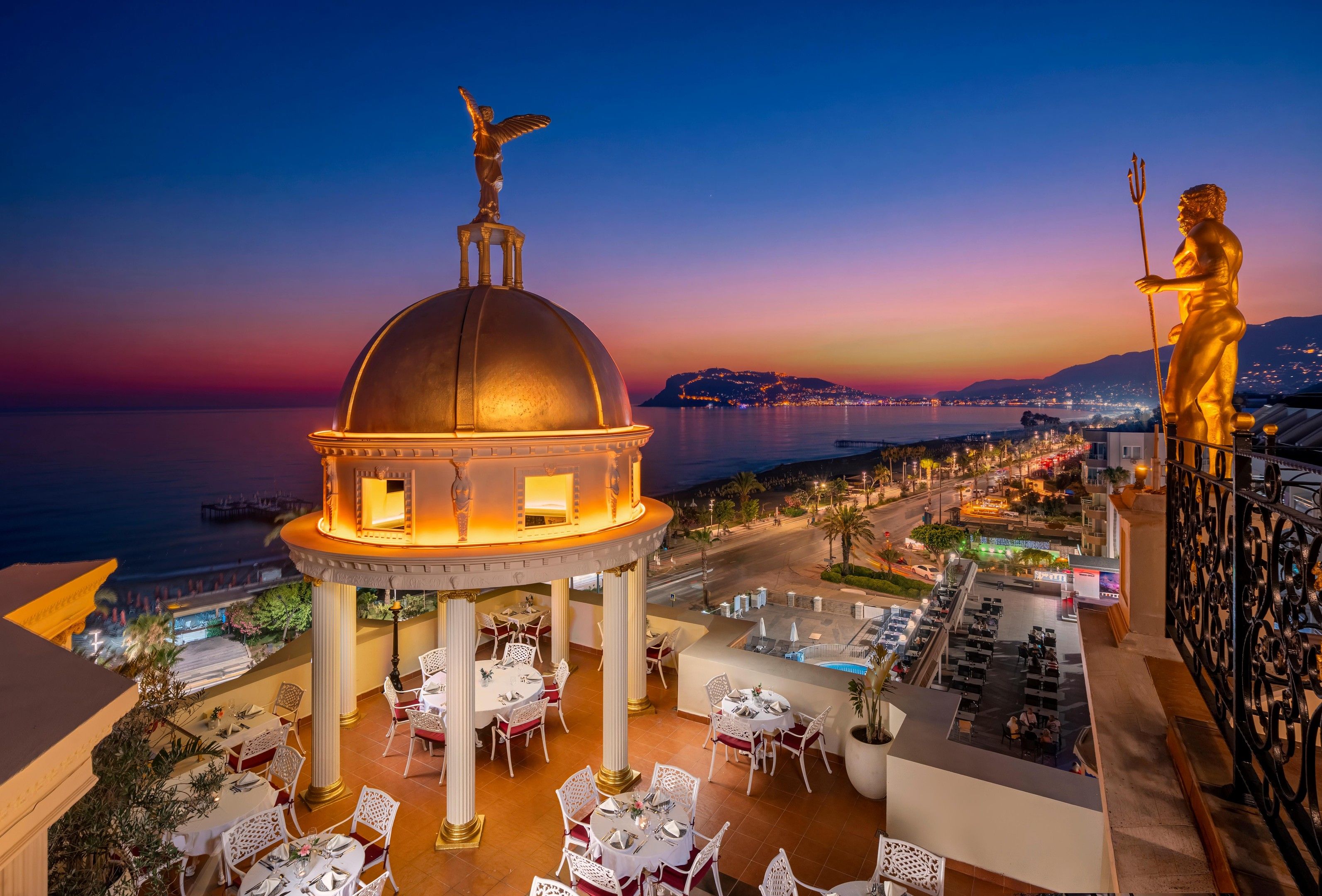 A domed structure with a statue on top, overlooking a coastal cityscape at dusk.