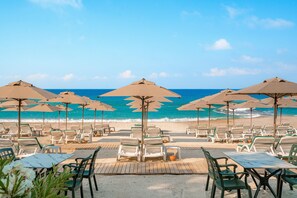 Un espace aménagé au bord de la plage, avec des parasols et des chaises longues donnant sur l’océan.