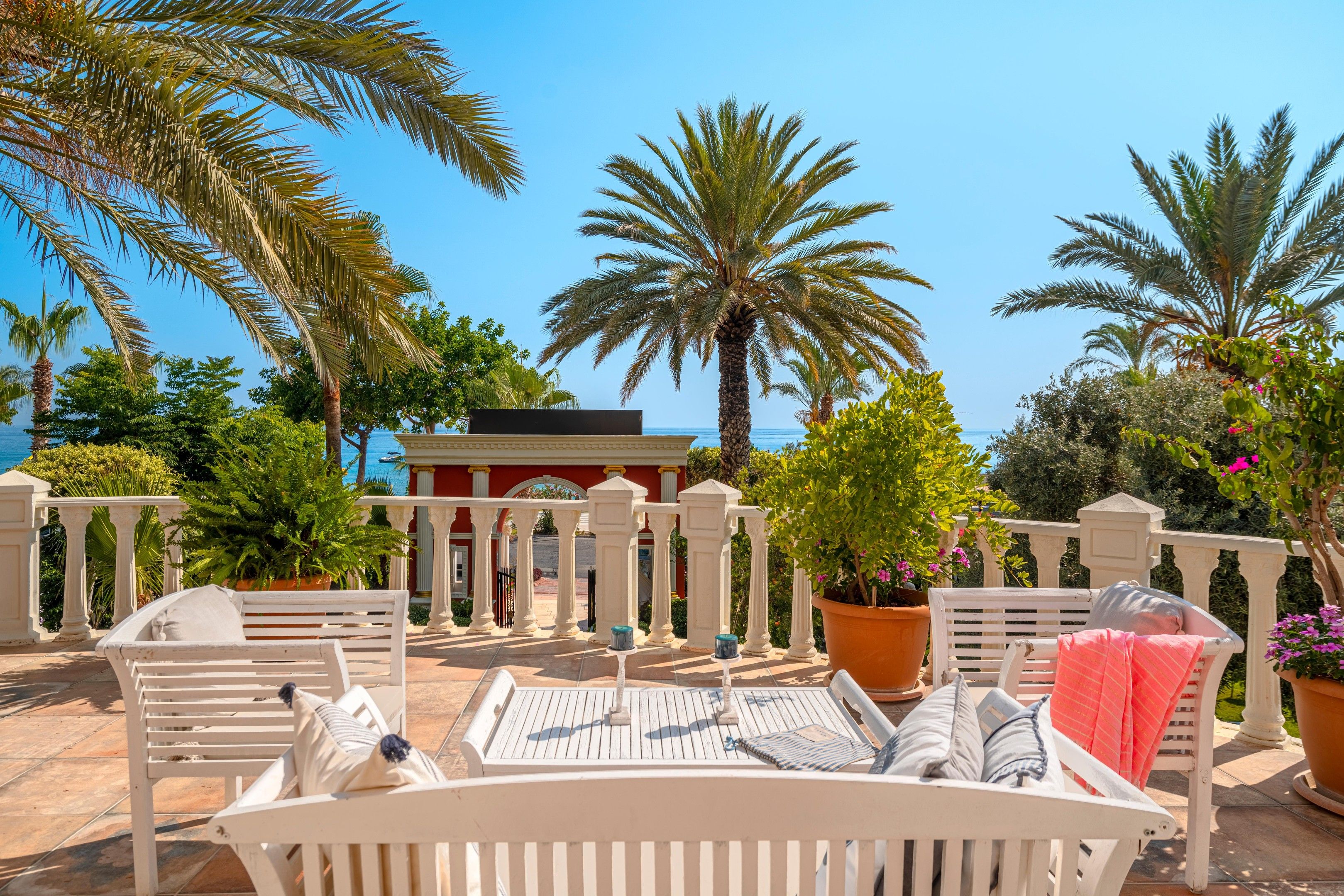 Une terrasse dotée de mobilier blanc, de palmiers et offrant une vue sur la mer.