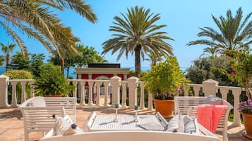 Une terrasse dotée de mobilier blanc, de palmiers et offrant une vue sur la mer.