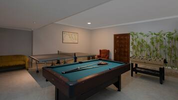 A pool table with billiard balls, a foosball table, and a sofa in a room with a wooden door and a map on the wall.