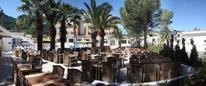 Un espacio al aire libre con mobiliario de mimbre, palmeras y un edificio al fondo.