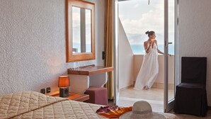 Une chambre d’hôtel avec un lit, une table de chevet avec une lampe, un miroir et une vue sur la mer, visible à travers une porte vitrée.