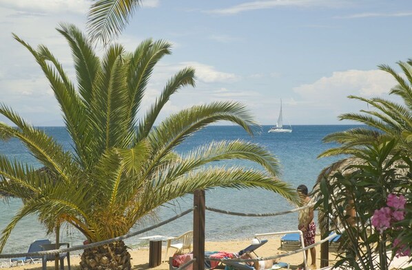 A beach with palm trees, a hammock, and a sailboat in the distance. - Long Beach Resort (Aigialeia)