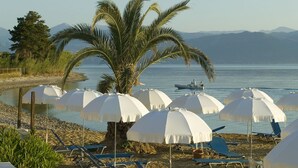 Une plage avec des parasols blancs, des palmiers et un bateau sur l’eau.