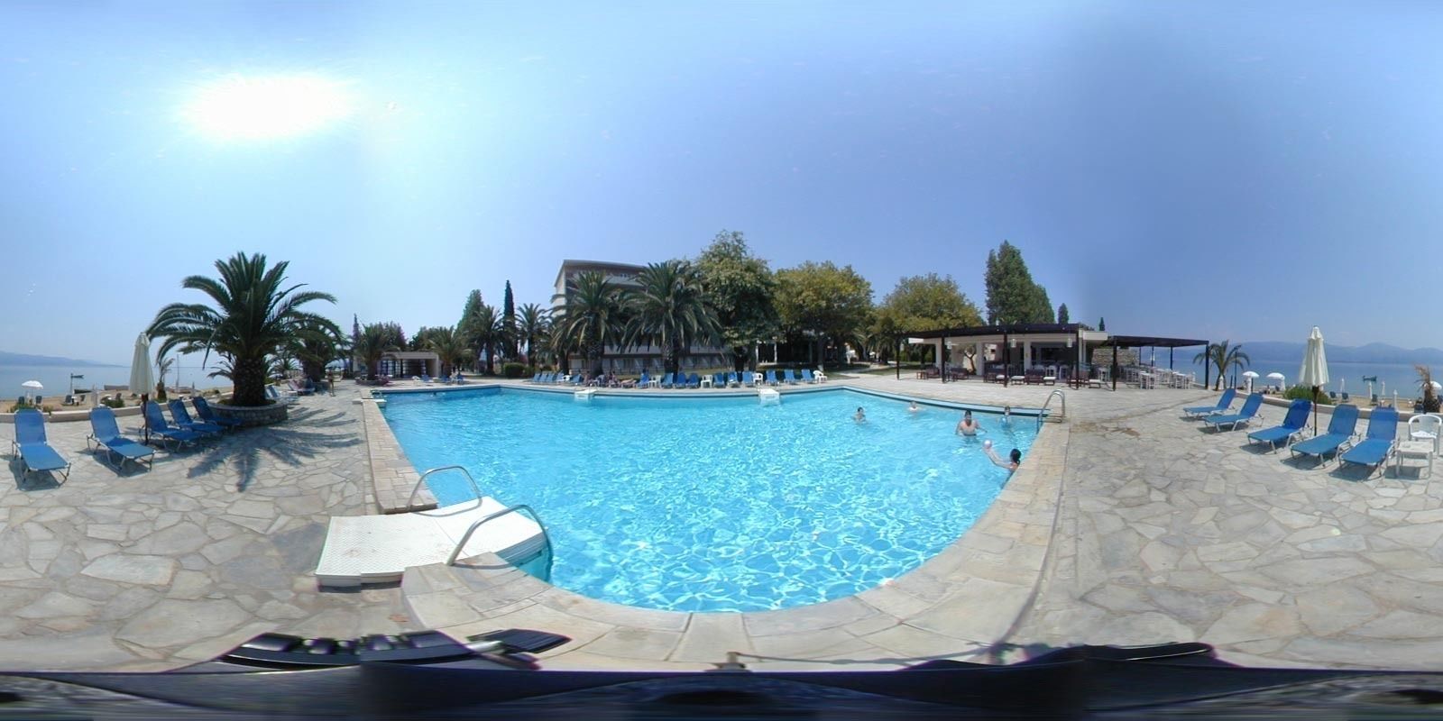 A swimming pool with clear blue water, surrounded by stone tiles and blue lounge chairs.