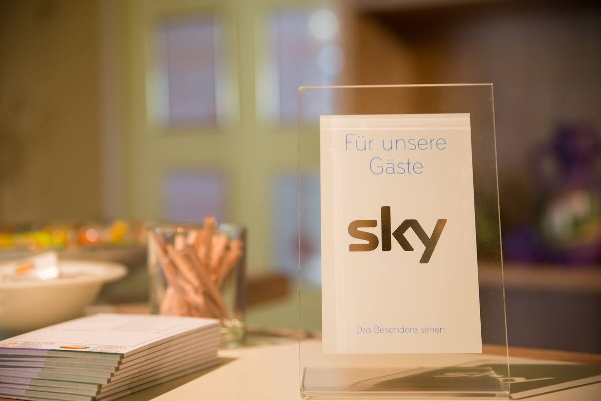 A sign with the word 'sky' and text in German, placed on a table with books and a glass container.