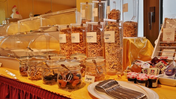A buffet area with various food options including jars of cereal, nuts, and fruits, as well as packaged snacks and condiments. - Hotel Toskana (Wiesbaden)