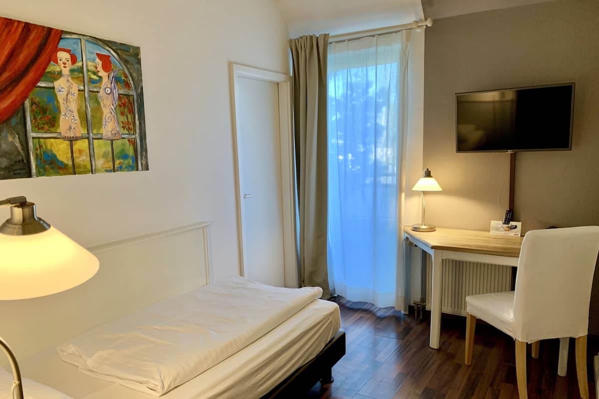 A hotel room with a bed, a desk with a chair, a TV, and a window with curtains.
