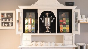 A tea display cabinet with a decorative top, containing various tea boxes and a large silver teapot. - Hotel Toskana (Wiesbaden)