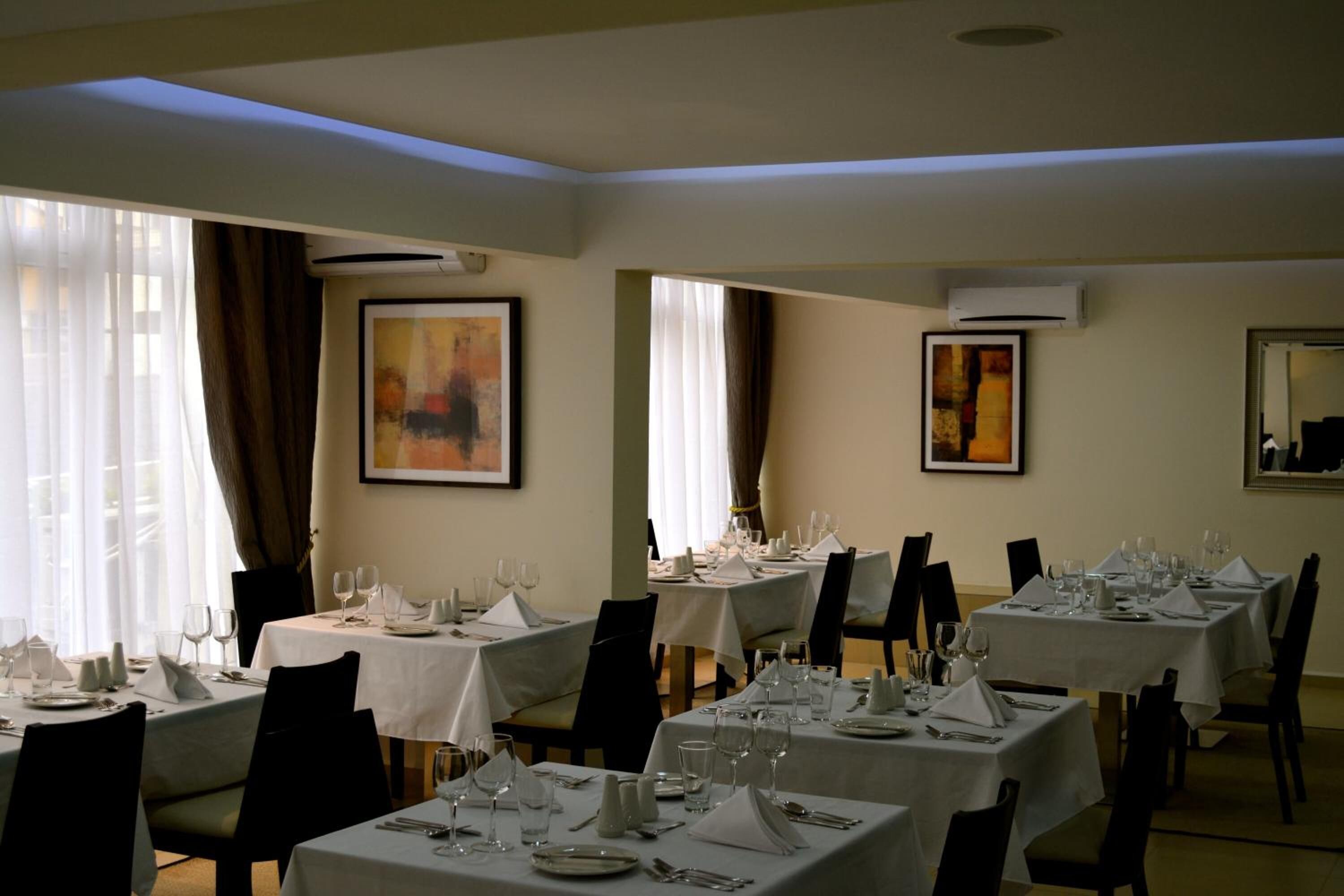 Un comedor con mesas dispuestas para el servicio, obras de arte enmarcadas en las paredes y unidades de aire acondicionado.