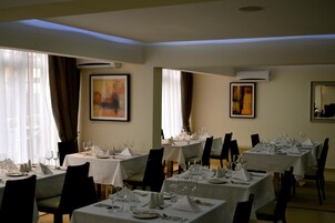 Un comedor con mesas dispuestas para el servicio, obras de arte enmarcadas en las paredes y unidades de aire acondicionado.