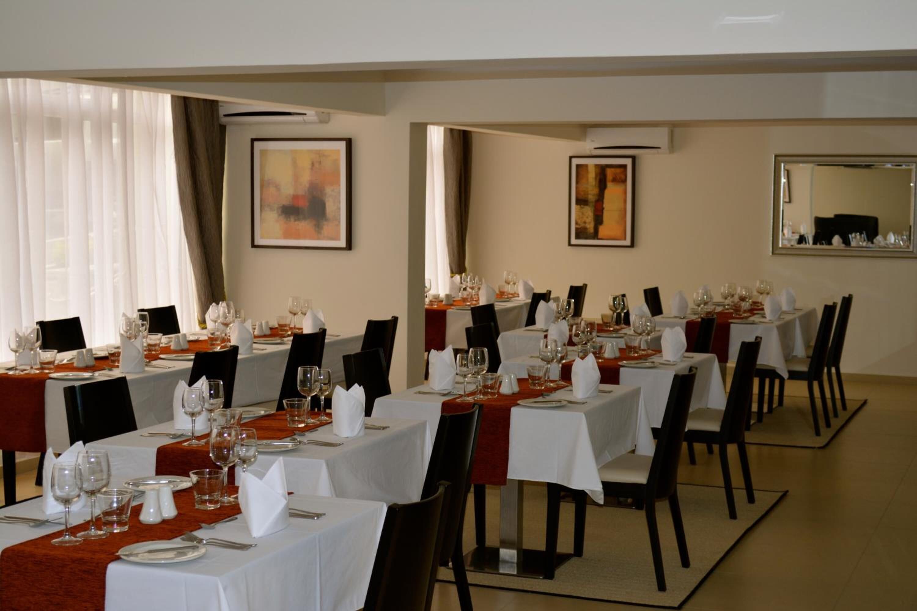 A dining area with multiple tables set for a meal, featuring white tablecloths, black chairs, and neatly arranged tableware.
