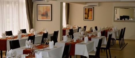 A dining area with multiple tables set for a meal, featuring white tablecloths, black chairs, and neatly arranged tableware.