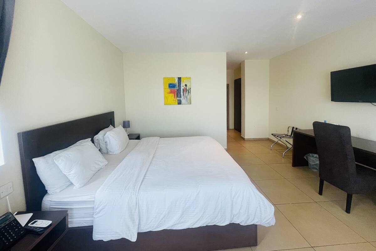 A hotel room with a large bed, a desk, a chair, a TV, and a painting on the wall.