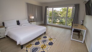 Ein Schlafzimmer mit einem großen Bett, einem Nachttisch mit Lampe, einem kleinen Schreibtisch mit Stuhl und einem großen Fenster mit Vorhängen.