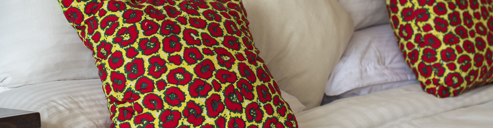 A bed with white bedding and two pillows with a red and yellow pattern.