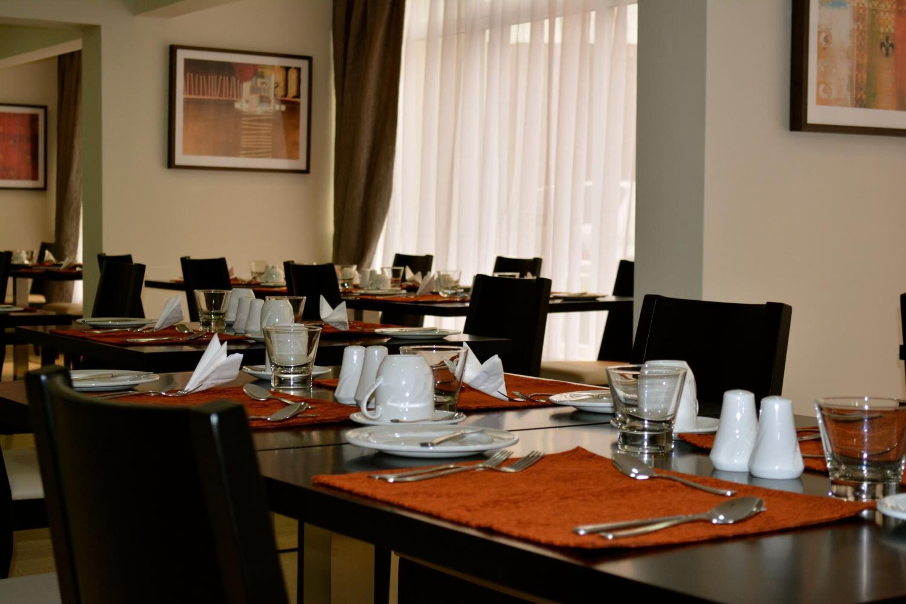A dining area with tables set for multiple guests, featuring placemats, cutlery, and glassware.