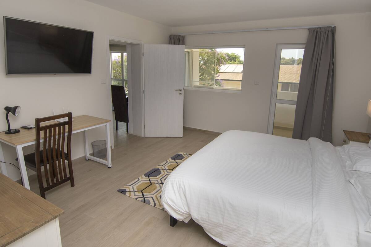 A hotel room with a bed, a desk with a chair, a television, and a window with curtains.