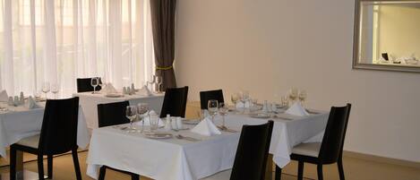 Un espace repas avec des tables dressées pour le repas, des chaises et une grande fenêtre agrémentée de rideaux.