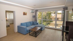 Ein modernes Wohnzimmer mit einem blauen Ecksofa, einem Holztisch und einem großen Fenster mit Blick ins Freie.