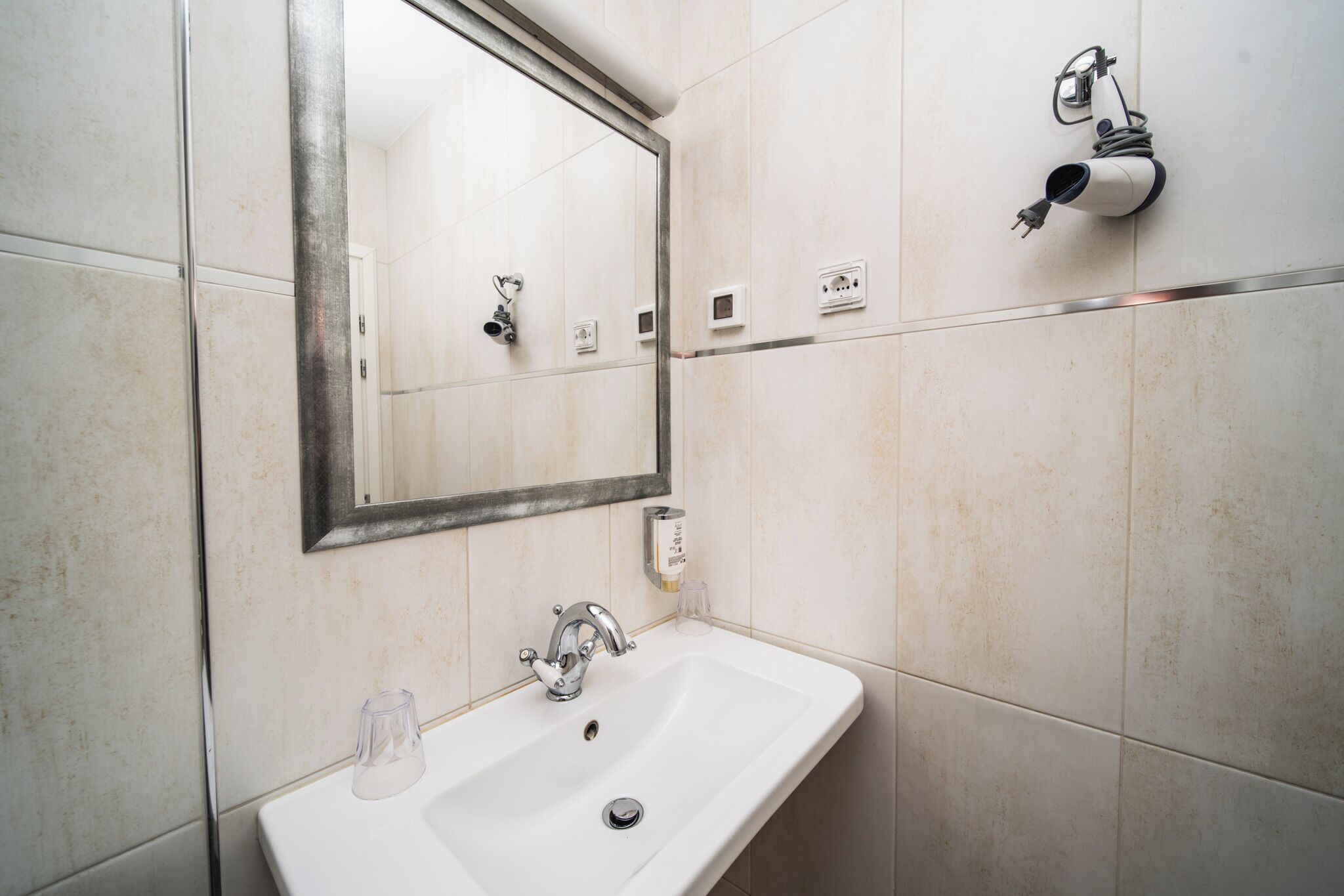 A bathroom with a sink, mirror, and towel dispenser.