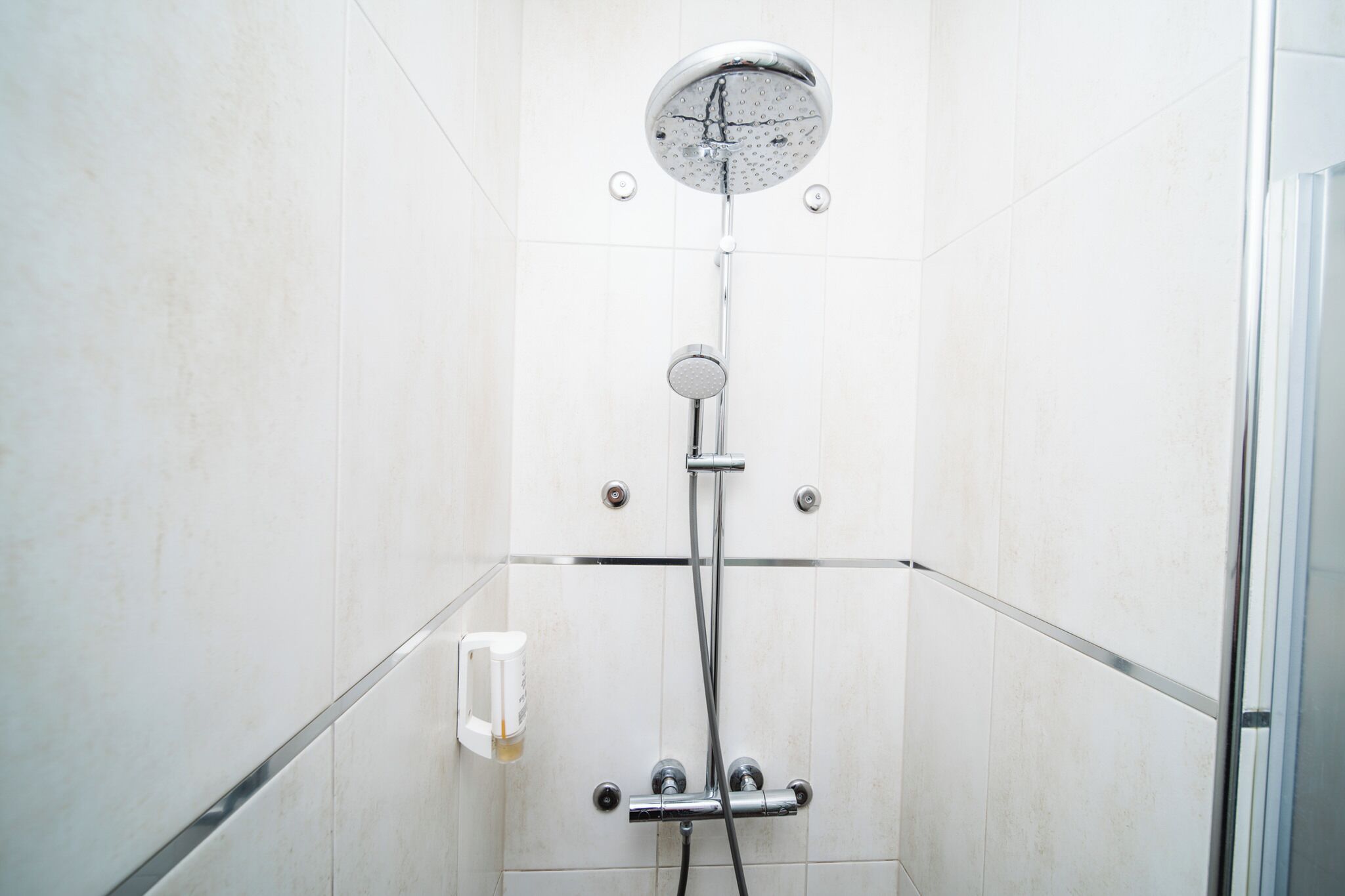 Une douche équipée d’un pommeau de douche à main, d’un robinet mural et d’un distributeur de savon.