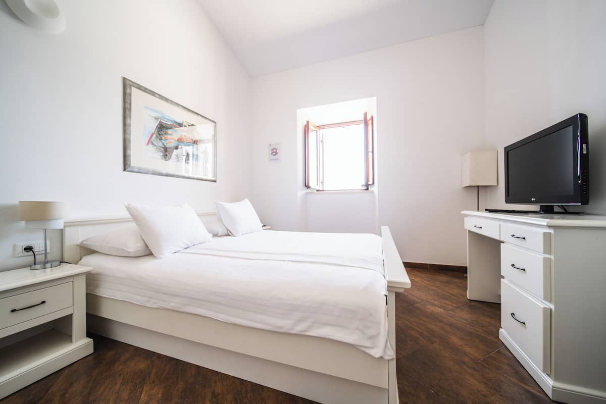 A bedroom with a bed, a TV, a desk, and a window.